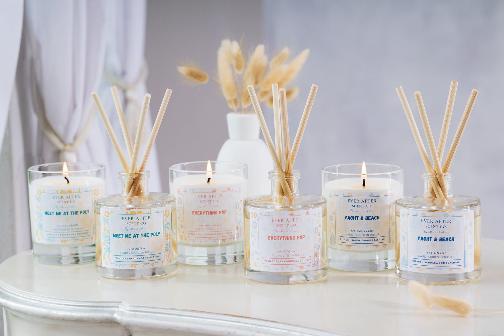 Collection of Ever After Scent candles and diffusers on a table with a neutral background. The scents include Meet me at the poly, Everything pop and Yacht & Beach.
