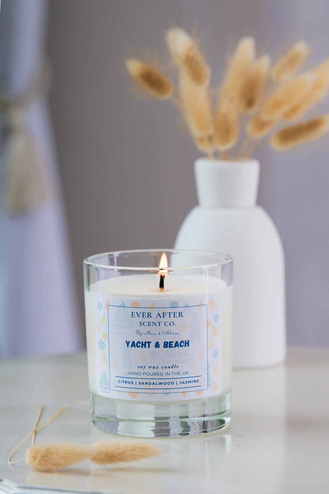 Glass candle labeled 'Yacht & Beach' by Ever After Scent Co. on a reflective surface with a blurred background.