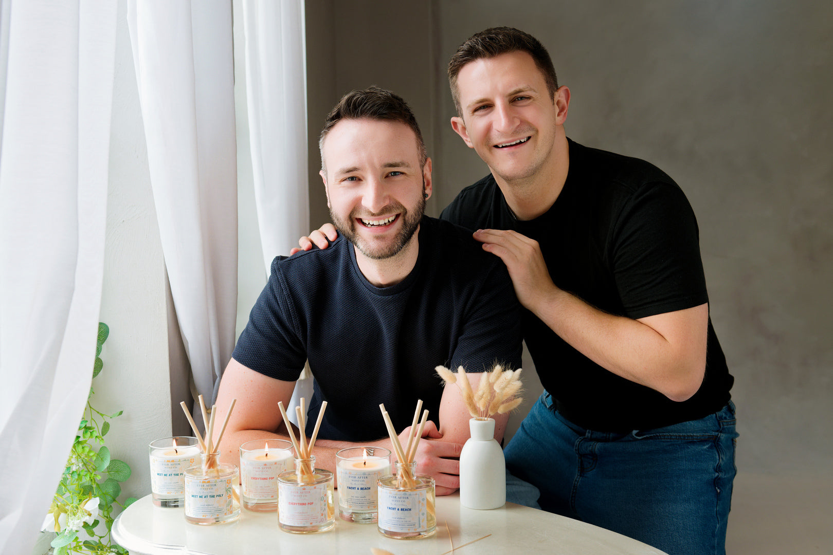 Max & Alex from Ever After Scent Co, posing in at a table with the collection of candles and reed diffusers inspired by Disney resort scents. 